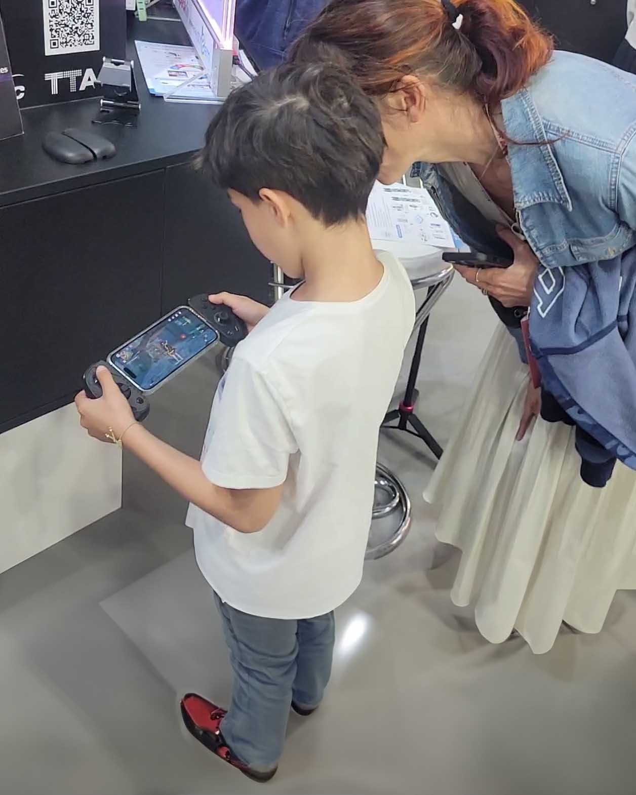 A little boy plays Genshin Impact with the Serafim S3. His mother is watching his gameplay near him.